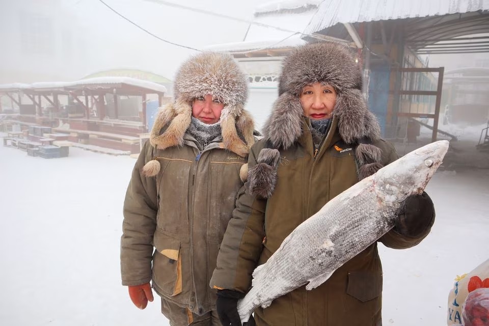 مچھلی فروش مرینا کریوولوتسکایا اور ماریانا یوگائی 15 جنوری 2023 کو روس کے یاکوتسک میں ایک ٹھنڈے دن کھلے بازار میں تصویر کے لیے پوز دے رہے ہیں۔— رائٹرز