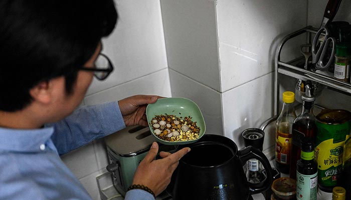 The photo taken on December 23, 2022 shows a Chinese medicine enthusiast Mex Yu pouring a plate of traditional herb medicine into a pot at his home in Beijing. — AFP