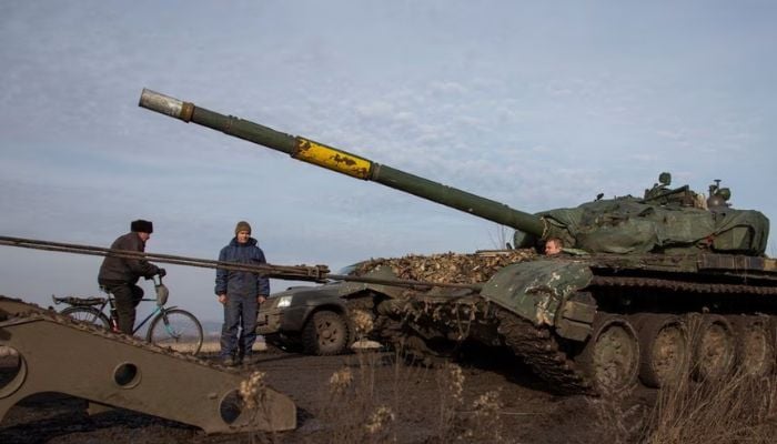 A Ukrainian serviceman looks on and a local resident rides a bicycle while a broken tank is pulled to a truck near the frontline town of Bakhmut, amid Russias attack on Ukraine, in Donetsk region, Ukraine January 20, 2023. — Reuters