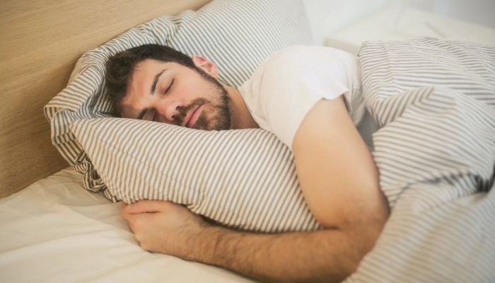 Photo of a man sleeping while he holds his pillow.— Pexels