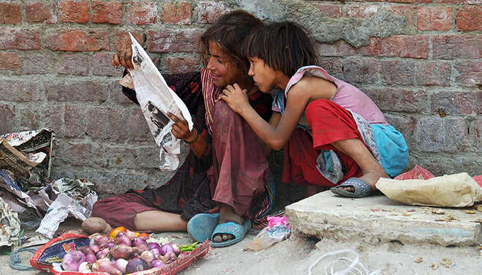 Young girls read a newspaper while selling vegetables in Lahore on June 12, 2022. — Online