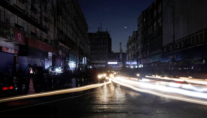 کراچی، پاکستان میں 23 جنوری 2023 کو ملک بھر میں بجلی کے بریک ڈاؤن کے دوران، گاڑیوں کی لائٹس مارکیٹ کے ساتھ ساتھ سڑک پر ہلکی لکیروں کا باعث بن رہی ہیں۔ - رائٹرز