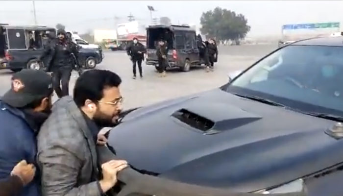 PTI leader Farrukh Habib tries to stop a police vehicle by standing in front of it.