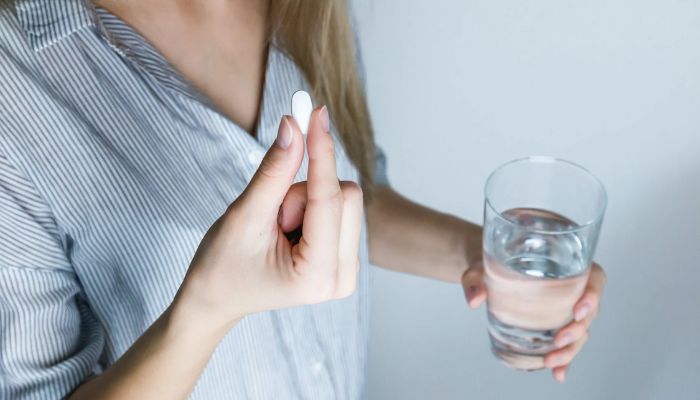 Woman holding half-full glass and white medicine pill. — Pexels