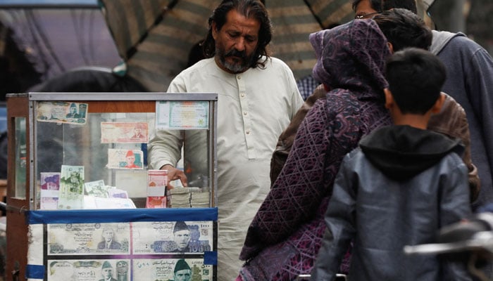 A currency broker stands near his booth, which is decorated with pictures of currency notes, while dealing with customers, along a road in Karachi, Pakistan January 27, 2023. — Reuters