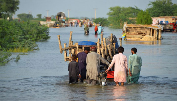 Men walk along a flooded road with their belongings, following rains and floods during the monsoon season in Sohbatpur, Pakistan. — Reuters/File