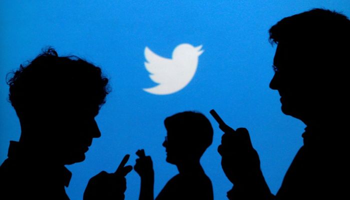 People holding mobile phones are silhouetted against a backdrop projected with the Twitter logo in this illustration picture taken September 27, 2013.— Reuters