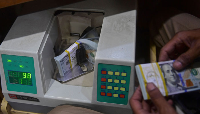 A currency dealer counting $100 bills in a machine in this undated photo. — AFP/File