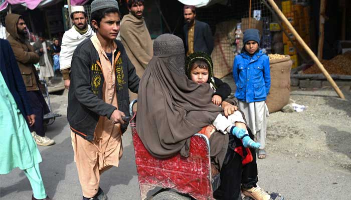 In this picture taken on February 2, 2023, an Afghan boy pushes a cart as he helps to transport a woman with a child before she crosses into Pakistan at the zero point Torkham border, in Nangarhar province. — AFP