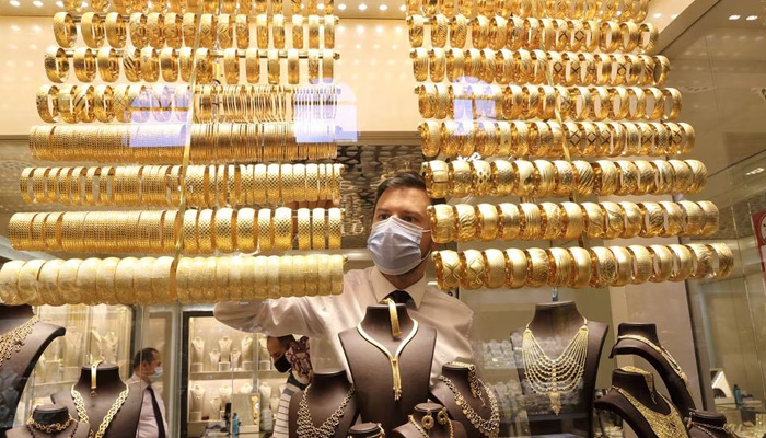 goldsmith wearing a protective face mask arranges golden bangles as the other talks to customers at a jewellery shop. — Reuters/File