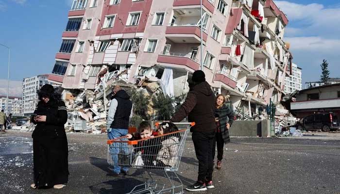 Children sit in a shopping cart near a collapsed building following an earthquake in Hatay, Turkey, February 7, 2023. — Reuters