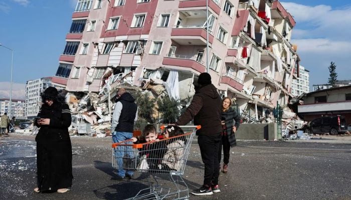 Children sit in a shopping cart near a collapsed building following an earthquake in Hatay, Turkey, February 7, 2023.— Reuters