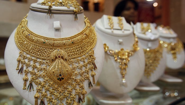 A saleswoman stands behind the showcased gold necklaces at a jewellery showroom. — Reuters