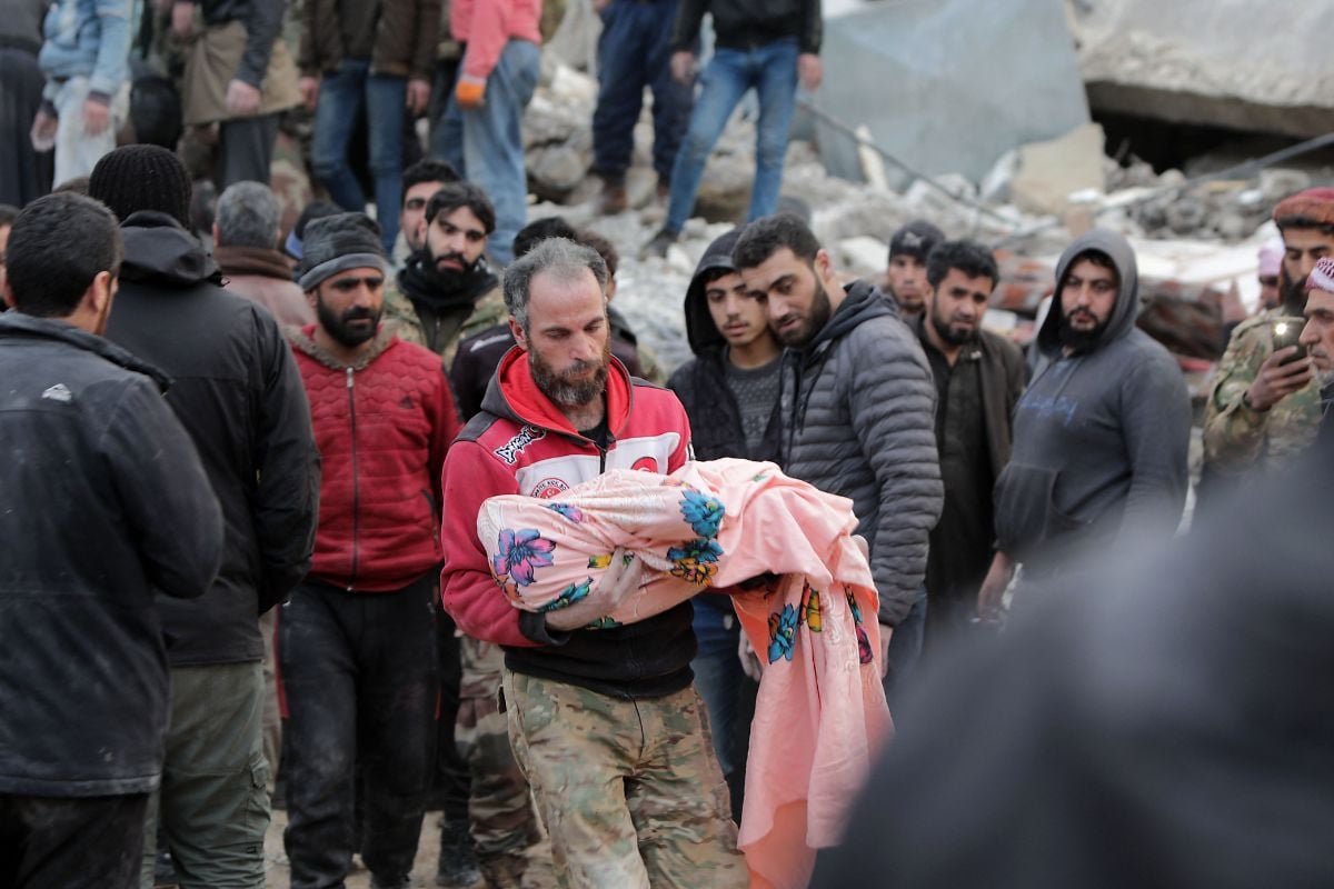 A Syrian man carries the body of a child after it was recovered from the rubble of a building on February 7 in the town of Jandairis.— AFP