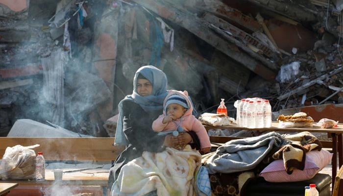 A woman holding a child sits by a collapsed building as search for survivors continues, in the aftermath of a deadly earthquake in Hatay, Turkey, February 10, 2023. — Reuters