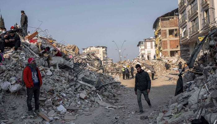 People stand on the rubble of a collapsed building during rescue operations in Hatay on February 12, 2023. — AFP