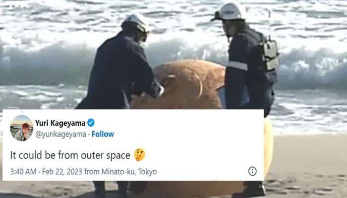 Two professionals inspecting the metal ball that washed up on a local beach in Japan, in this still taken from a video.— Twitter/NHK