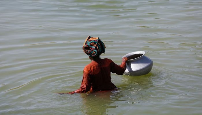A displaced woman wades through flood water with a water pot, following rains and floods during the monsoon season in Sehwan, on September 16, 2022. — Reuters