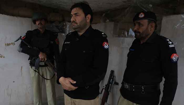 Jameel Shah, 40, stands between two police officers as they observe their surroundings, at Sarband Police Station on the outskirts of Peshawar, February 9, 2023. — Reuters