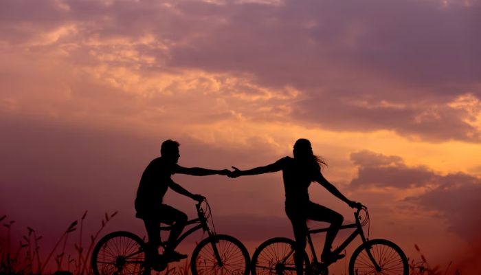 Silhouette of a man and a woman cycling and holding hands. — Unsplash