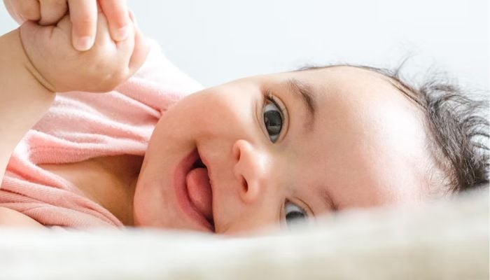 A baby smiling while laying on a bed.— Unsplash