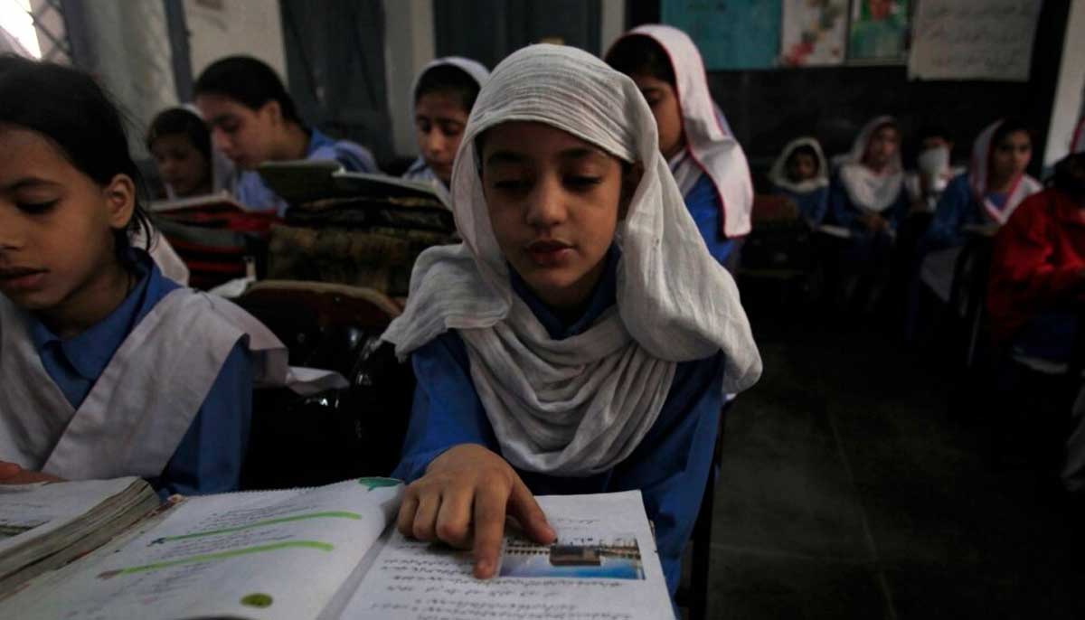 A girl reads a book while attending her daily class with others at a government school in Peshawar, Oct. 29, 2014. — Reuters