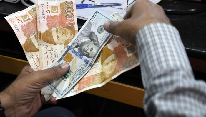 A foreign currency dealer shows a dollar bill and Pakistani rupee notes at a shop in Karachi. — Online/File