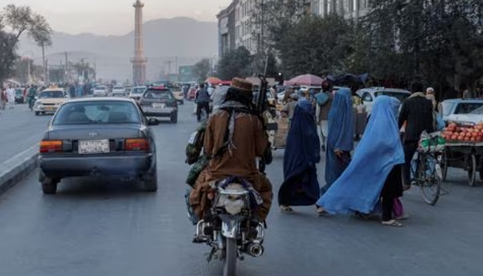 A group of women wearing burqas crosses the street as members of the Taliban drive past in Kabul, Afghanistan October 9, 2021. — Reuters