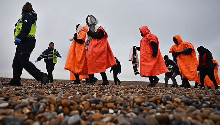 A British Immigration Enforcement officer (L) and an Interforce security officer (2L), escort migrants on December 09, 2022. —AFP/file