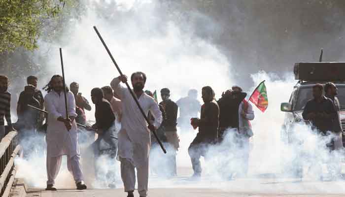 Supporters of former prime minister Imran Khan, react amid tear gas smoke fired by the police to disperse them during clashes ahead of an election campaign rally, in Lahore, Pakistan March 8, 2023. —Reuters