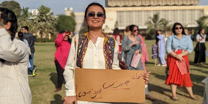 A young girl smiles for the camera showing a placard which reads that she isnt anything but a human being, at Burns Garden where Aurat March was held on March 12, 2023. — Photo by author