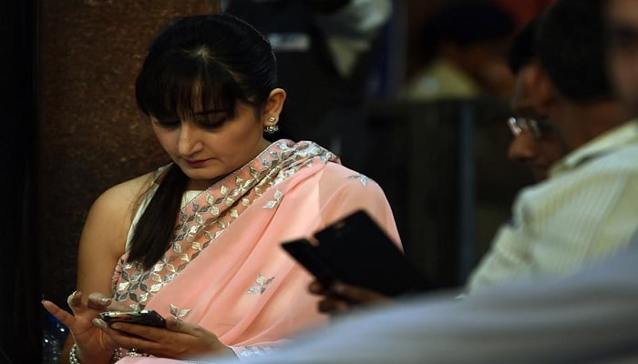 Indian commuters use their smartphones while waiting for the trains at Mumbais central railway station.— AFP/File