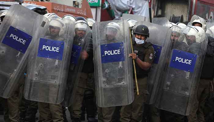 14 مارچ، 2023 کو لاہور، پاکستان میں، ان کے گھر کے باہر ان کی ممکنہ گرفتاری سے قبل جھڑپوں کے دوران، پی ٹی آئی چیئرمین عمران خان کے حامیوں کی جانب سے پتھراؤ سے بچنے کے لیے پولیس اہلکار ہنگامہ آرائی میں ڈھال کے پیچھے پہرہ دے رہے ہیں۔ - رائٹرز