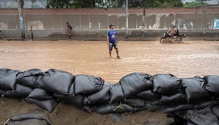 People wade through water flooding the main access road to Lima following heavy rains in Chaclacayo, east of Lima, Peru on March 15, 2023. AFP