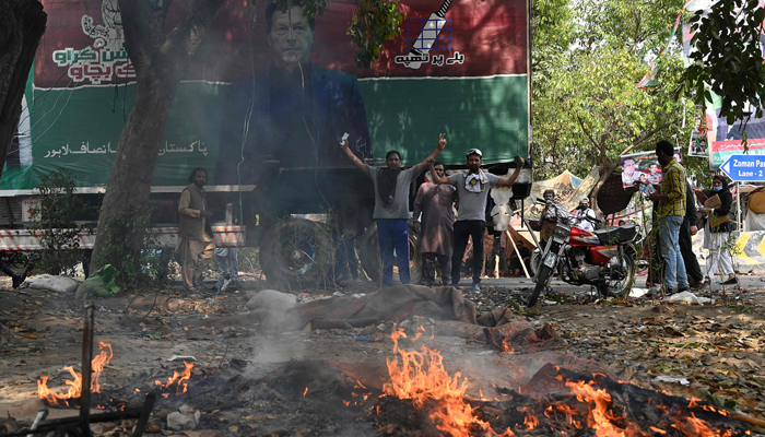 Supporters of former Pakistans prime minister Imran Khan gesture along a road blocked near Khans residence to prevent officers from arresting him, in Lahore on March 15, 2023. — AFP