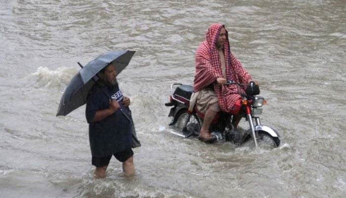 An undated image of men wading through a flooded road in Karachi — Reuters