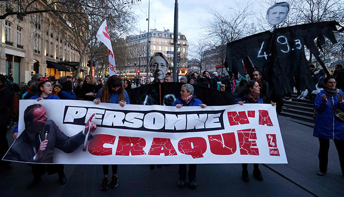 Protesters hold a banner and placards depicting French Labour Minister Olivier Dussopt (L), French Prime Minister Elisabeth Borne (C) and French President Emmanuel Macron at Place de la Republique during a demonstration, a few days after the government pushed a pensions reform through parliament without a vote, using the article 49.3 of the constitution, in Paris on March 21, 2023. AFP