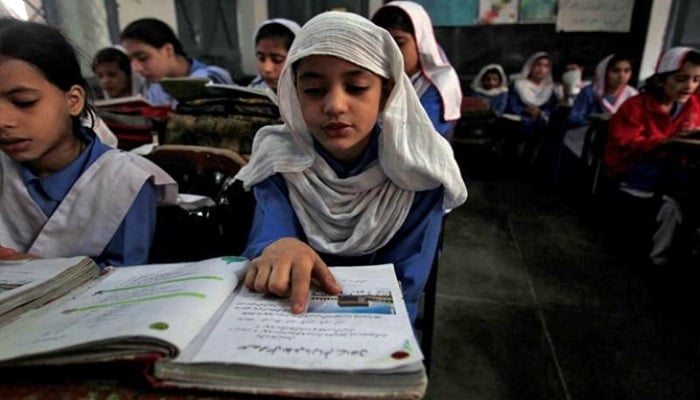 In this file photo, a girl reads a book while attending her daily class with others at a government school.— Reuters