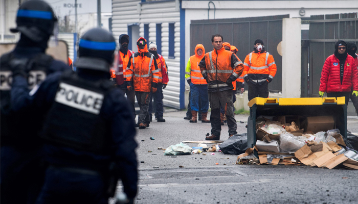 Police officers look at dockers blocking the entrance of the oil depot in Lorient, western France, on March 22, 2023, a day after the oil depot of Lorient was unblocked by the police. — AFP