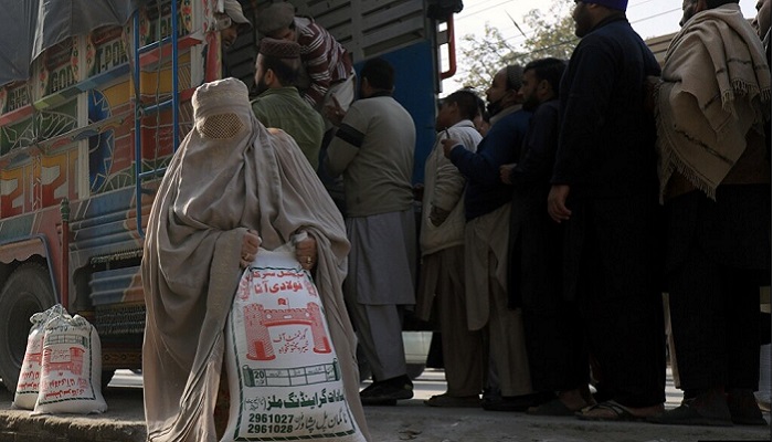 A woman, clad in burqa, carries a sack of flour, purchased at a subsidised rate from a truck along a road in the northwestern city of Peshawar. — Reuters