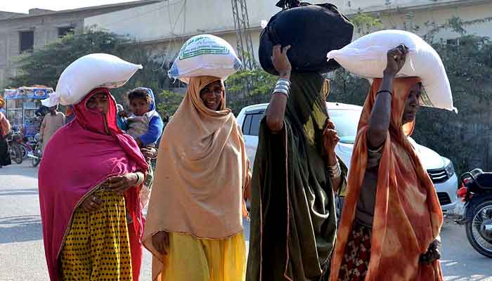 Women going back home after purchasing subsidised flour from a delivery truck near Niaz Stadium, Hyderabad. —APP/File