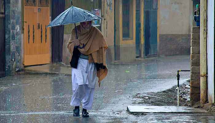 An old man covering himself with an umbrella during rain in Peshawar on March 24, 2023. — APP