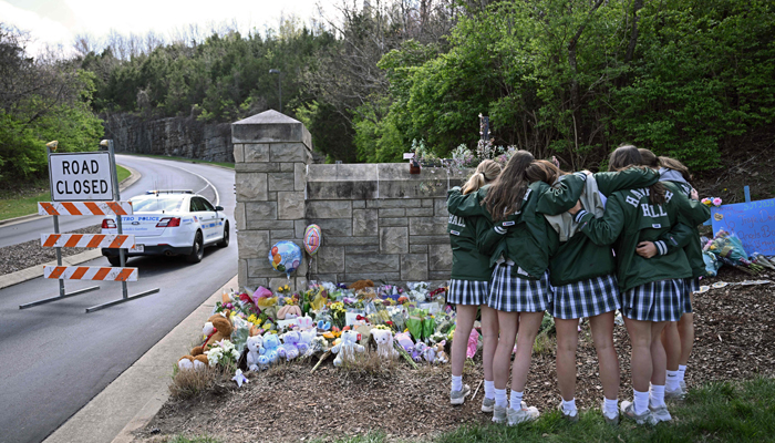 Girls embrace in front of a makeshift memorial for victims by the Covenant School building at the Covenant Presbyterian Church following a shooting, in Nashville, Tennessee, March 28, 2023. — AFP