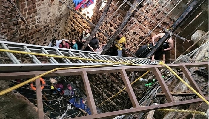 Rescue workers busy pulling the dead and the injured out of the collapsed stepwell. — AFP