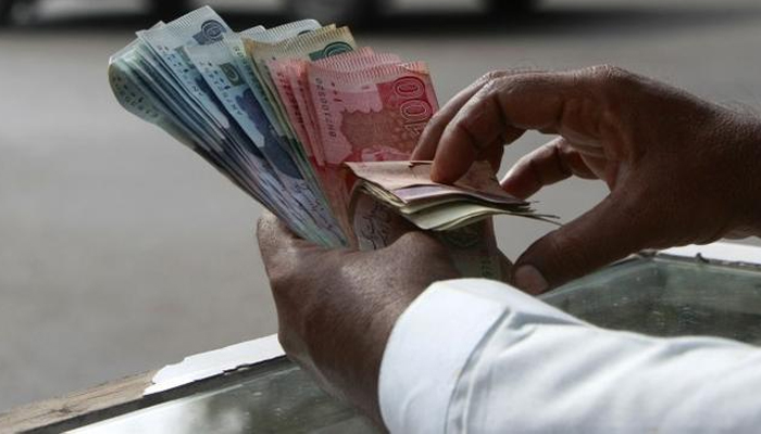 A money changer counts Pakistani rupee notes in Karachi in this undated photo. — Reuters/File