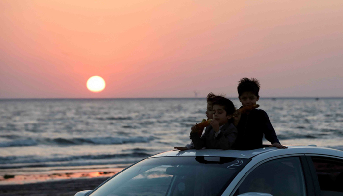 Children eat corn on cob as they ride on a car against the setting sun on New Years Eve in Karachi on Dec 31, 2022. — Reuters