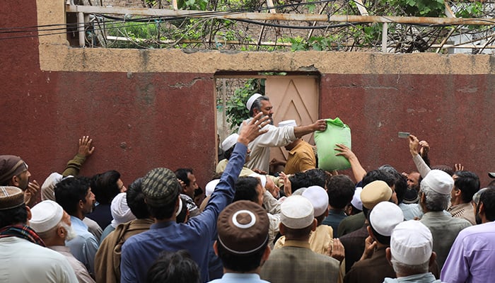 People gather to receive sacks of free flour at a distribution point in Peshawar, on March 30, 2023. — Reuters