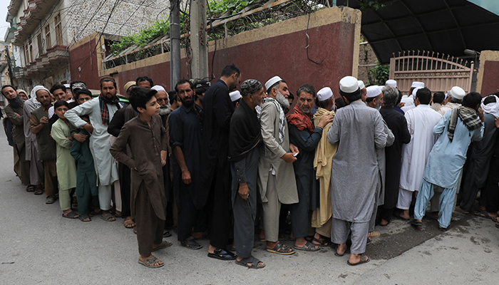 People stand in queue to receive sacks of free flour, at a distribution point in Peshawar, on March 30, 2023. — Reuters