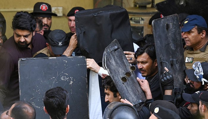 Security personnel use bullet proof shields to protect former prime minister Imran Khan (C) as he arrives at the high court in Islamabad on March 27, 2023. — AFP