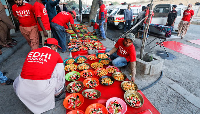ایدھی فاؤنڈیشن کے رضاکار، ایک غیر منافع بخش سماجی بہبود کے پروگرام، 3 اپریل 2023 کو کراچی میں ایک سڑک پر لوگوں کے لیے افطاری کے لیے کھانے کی پلیٹوں کا بندوبست کر رہے ہیں۔ — رائٹرز